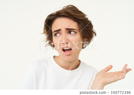 Portrait of disappointed young woman complaining, holding hand sideways, talking, expresses dislike and irritation, standing over white background Portrait of disappointed young woman complaining, holding hand sideways, talking, expresses dislike and irritation, standing over white background 108772386