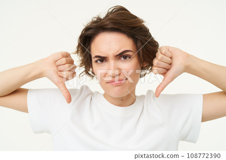 Close up portrait, face of young woman that is showing thumbs down, dislike, do not recommend gesture, express negative feedback, isolated over white background 108772390