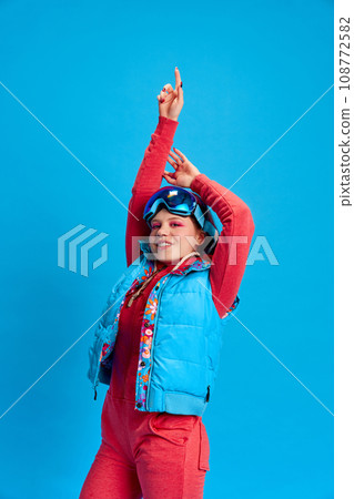 Young girl with bright makeup and pricing, wearing winter colorful clothes against blue studio background Young girl with bright makeup and pricing, wearing winter colorful clothes against blue studio background 108772582