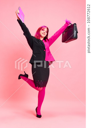 Success. Young girl with bright hair and colorful suit celebrating promotion against pink studio background. Emotions Success. Young girl with bright hair and colorful suit celebrating promotion against pink studio background. Emotions 108772612