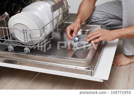 handsome man putting detergent tablet into dishwasher in kitchen handsome man putting detergent tablet into dishwasher in kitchen 108772958