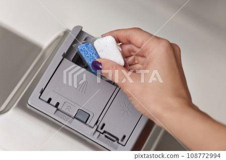female hand puts dishwasher tablet into open automatic built-in dishwasher machine. Close-up 108772994