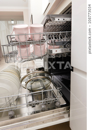 Open built-in dishwasher machine with clean cutlery, dishes, plates in white modern kitchen Open built-in dishwasher machine with clean cutlery, dishes, plates in white modern kitchen 108773034