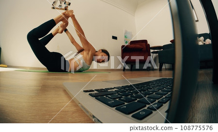 A slim woman having an online yoga class at home 108775576