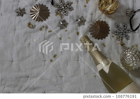 Moody new year party, celebration banner. Bottle of champagne wine, vintage Christmas balls, baubles and golden star confetti decor. Muslin tablecloth. Birthday, anniversary concept. Flat lay, top 108776191