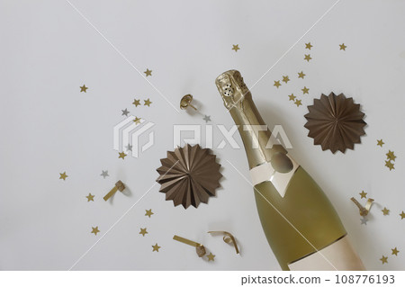 Happy new year still life. Bottle of champagne wine and star shape golden confetti isolated on beige table background. Birthday, party celebration and anniversary. Alcoholic drink. Moody flat lay, top 108776193