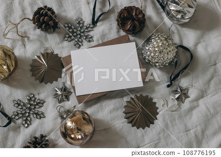 Moody Christmas stationery. Blank paper greeting card, invitation mockup. Vintage glass baubles, balls, pine cones on muslin blanket. Decorative winter composition on table. Festive holidays banner. Moody Christmas stationery. Blank paper greeting card, invitation mockup. Vintage glass baubles, balls, pine cones on muslin blanket. Decorative winter composition on table. Festive holidays banner. 108776195