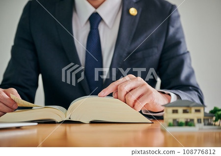 A male lawyer researches the problem of empty houses in his parents' home by looking at the complete set of six law books. A male lawyer researches the problem of empty houses in his parents' home by looking at the complete set of six law books. 108776812
