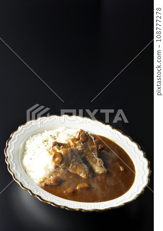 Hot curry rice with bone-in chicken is photographed against a black background Hot curry rice with bone-in chicken is photographed against a black background 108777278