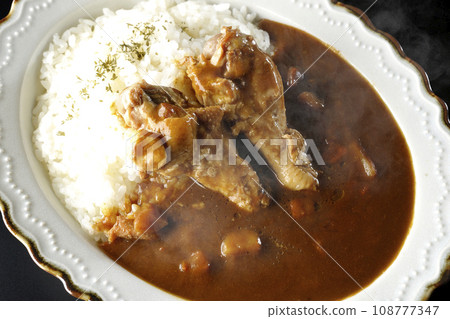 Overhead shot of hot curry rice with bone-in chicken against a black background 108777347