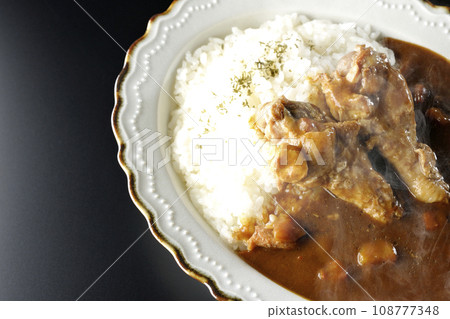Overhead shot of hot curry rice with bone-in chicken against a black background 108777348