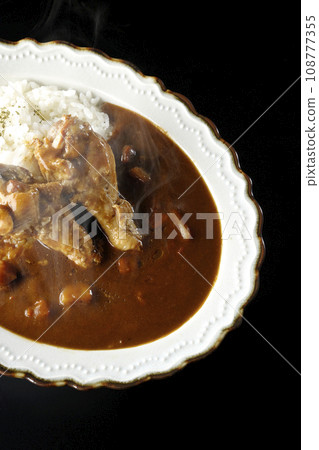 Overhead shot of hot curry rice with bone-in chicken against a black background Overhead shot of hot curry rice with bone-in chicken against a black background 108777355