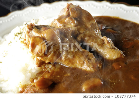 Hot curry rice with bone-in chicken is photographed against a black background Hot curry rice with bone-in chicken is photographed against a black background 108777374