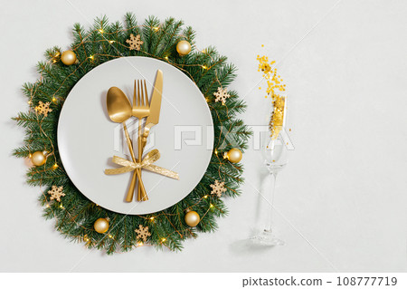 Festive table setting with Christmas wreath and golden decorations on white background with copy space. Happy new year. Space for text. Top view, flat lay. Festive table setting with Christmas wreath and golden decorations on white background with copy space. Happy new year. Space for text. Top view, flat lay. 108777719