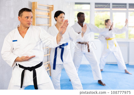 Middle-aged man attendee of karate classes practicing kata standing in row with others 108777975