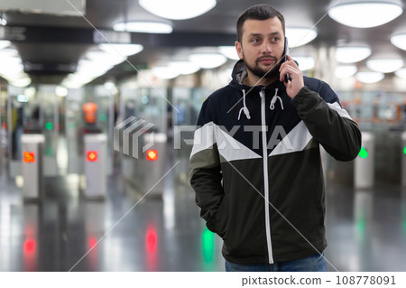 Man talking on phone at subway station with tickets barriers in background Man talking on phone at subway station with tickets barriers in background 108778091