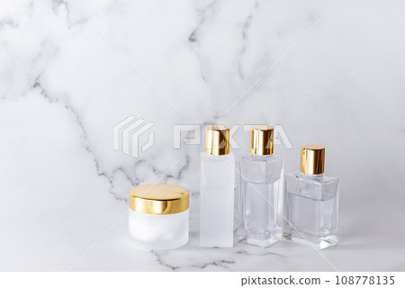 大理石背景上排列著帶有金蓋的玻璃化妝品瓶 108778135