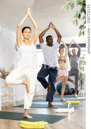 Happy woman in sportswear exercising with group active multinational people during yoga class in fitness center, standing in 108778151