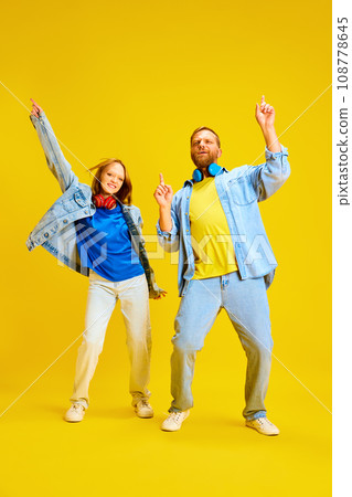 Overjoyed father and daughter, parent and kid dressed style denim outfit and have fun, listening music and dancing isolated yellow background. 108778645