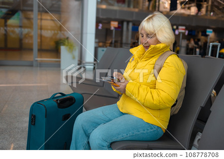 Airport senior 60s woman on smart phone at gate sitting in terminal hall while waiting for her flight.  108778708