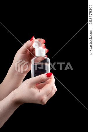 A plastic bottle with hand sanitizer in the palms of a young woman on a dark background. Health concept. 108779303