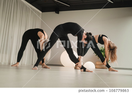 A group of girls in black doing yoga poses indoors. Women are engaged in fitness A group of girls in black doing yoga poses indoors. Women are engaged in fitness 108779863