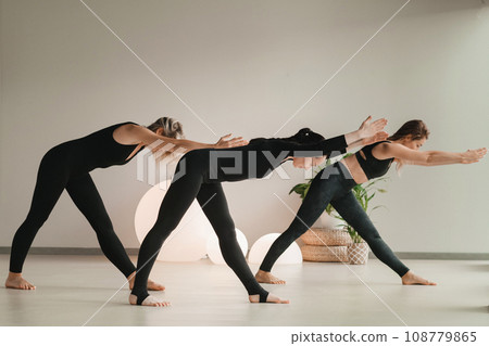 A group of girls in black doing yoga poses indoors. Women are engaged in fitness A group of girls in black doing yoga poses indoors. Women are engaged in fitness 108779865