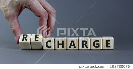 Charge or recharge symbol. Businessman turns wooden cubes and changes the word 'charge' to 'recharge'. Beautiful grey table, grey background. Business charge or recharge concept. Copy space. 108780076