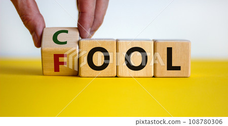 Do not be a fool just play cool symbol. Male hand turns wooden cubes and changes the word 'fool' to 'cool' on yellow table, white background, copy space. Business and fool or cool concept. 108780306