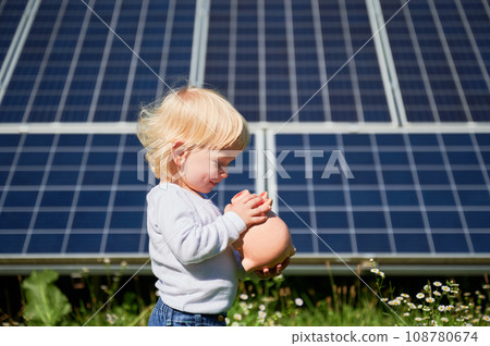 Little child saving money in piggy bank on background of solar panels. Smiling kid happy that he has some cash in his moneybox. Small boy learning about saving money for future. 108780674