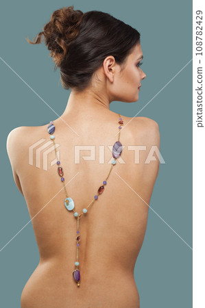 Stylish brunette female model with sautoir necklace on her back on blue background. Stylish brunette female model with sautoir necklace on her back on blue background. 108782429