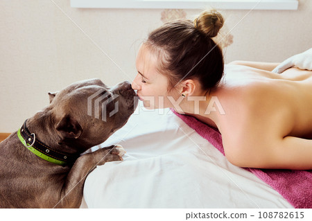 Young woman kisses her dog while lying on massage table in massage parlor. 108782615