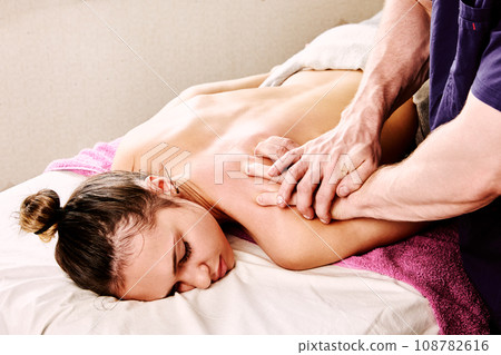 Back massage in spa beauty salon for young Caucasian woman, male masseur kneads muscles near neck. Back massage in spa beauty salon for young Caucasian woman, male masseur kneads muscles near neck. 108782616