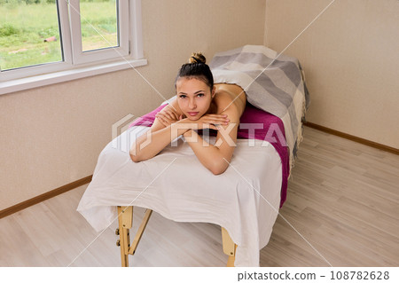 Massage table with European woman in her 20s who is lying on her stomach. Massage table with European woman in her 20s who is lying on her stomach. 108782628