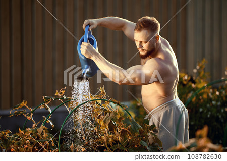 Using garden tool, watering can, man waters beds with cucumbers. Using garden tool, watering can, man waters beds with cucumbers. 108782630