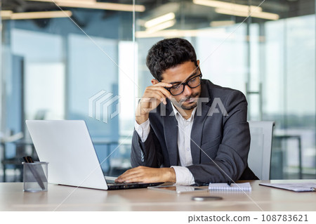 Tired male office worker sitting at desk in front of laptop at desk, tired from a lot of work, burnout, headache. Tired male office worker sitting at desk in front of laptop at desk, tired from a lot of work, burnout, headache. 108783621