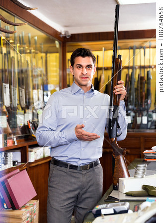 Handsome adult male owner of hunting shop offering rifle Handsome adult male owner of hunting shop offering rifle 108784658
