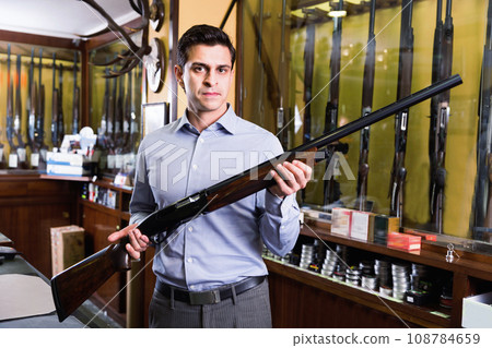 Handsome adult male in hunting shop with rifle in hands 108784659