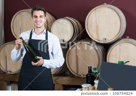 seller in apron holding bottle of wine. 108784824