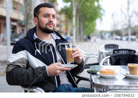 Young man traveler enjoying cocoa with donut in street cafe Young man traveler enjoying cocoa with donut in street cafe 108784832