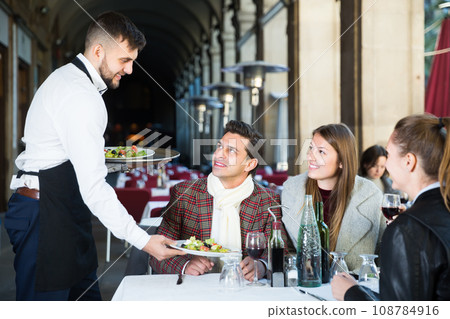 polite waiter serving guests at terrace restaurant 108784916