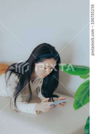 坐在沙發上玩智慧型手機的年輕女子 坐在沙發上玩智慧型手機的年輕女子 108785256