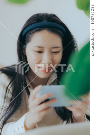 Young woman sitting on the sofa and playing with a smartphone 108785258