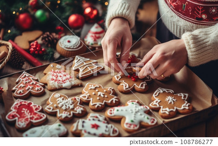 Woman decorating christmas gingerbread cookies with icing sugar on wooden background Woman decorating christmas gingerbread cookies with icing sugar on wooden background 108786277