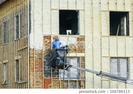 Technician spraying thermal insulation foam layer on the exterior wall using plural component gun for polyurethane foam Technician spraying thermal insulation foam layer on the exterior wall using plural component gun for polyurethane foam 108786315