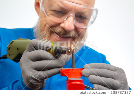 Bearded man mechanic processes metal with an engraving drill. 108787387