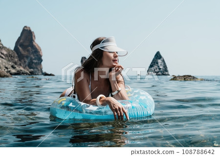 Woman summer sea. Happy woman swimming with inflatable donut on the beach in summer sunny day, surrounded by volcanic mountains. Summer vacation concept. Woman summer sea. Happy woman swimming with inflatable donut on the beach in summer sunny day, surrounded by volcanic mountains. Summer vacation concept. 108788642