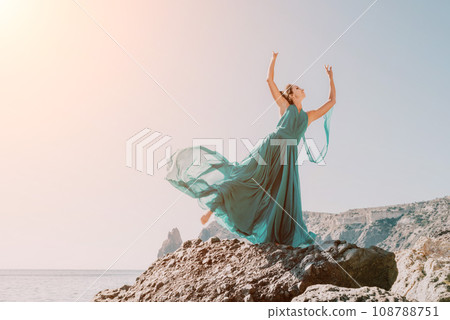 Side view a Young beautiful sensual woman with black hair in a long mint dress posing on a beach with calm sea bokeh lights on sunny day. Girl on the nature on blue sky background. Fashion photo 108788751