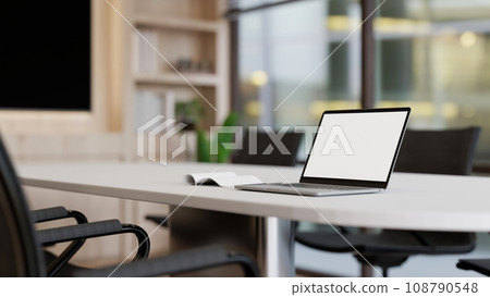 A white-screen laptop mockup on a white meeting table in a modern, minimalist meeting room. A white-screen laptop mockup on a white meeting table in a modern, minimalist meeting room. 108790548
