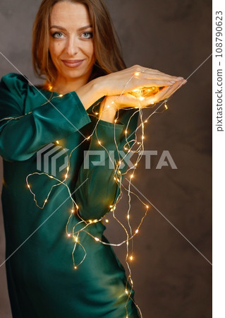 Portrait of a young woman celebrating Christmas Eve. Model posing for a photo. Woman wearing green dress. Portrait of a young woman celebrating Christmas Eve. Model posing for a photo. Woman wearing green dress. 108790623